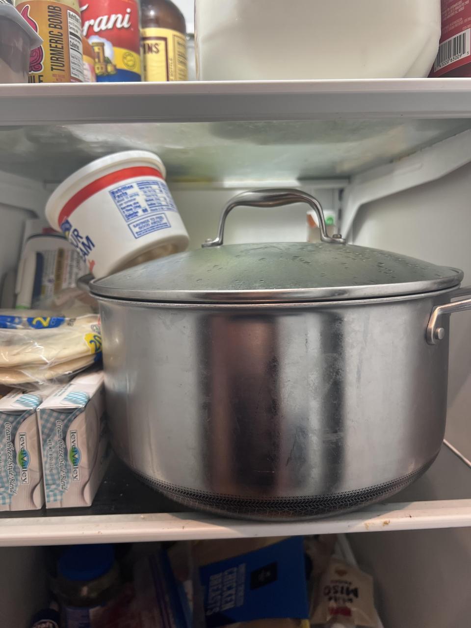 A pot with a lid inside a refrigerator with various food containers and bottles