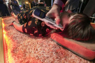 In this Tuesday, Aug. 6, 2019, photo, Dr. Vladimir Turovskiy, from the Carillon Miami Wellness Resort, uses electronic acupuncture on a woman lying on a warmed bed of Himalayan salt and quartz, during the 2019 International Spa Association event, in New York. (AP Photo/Richard Drew)