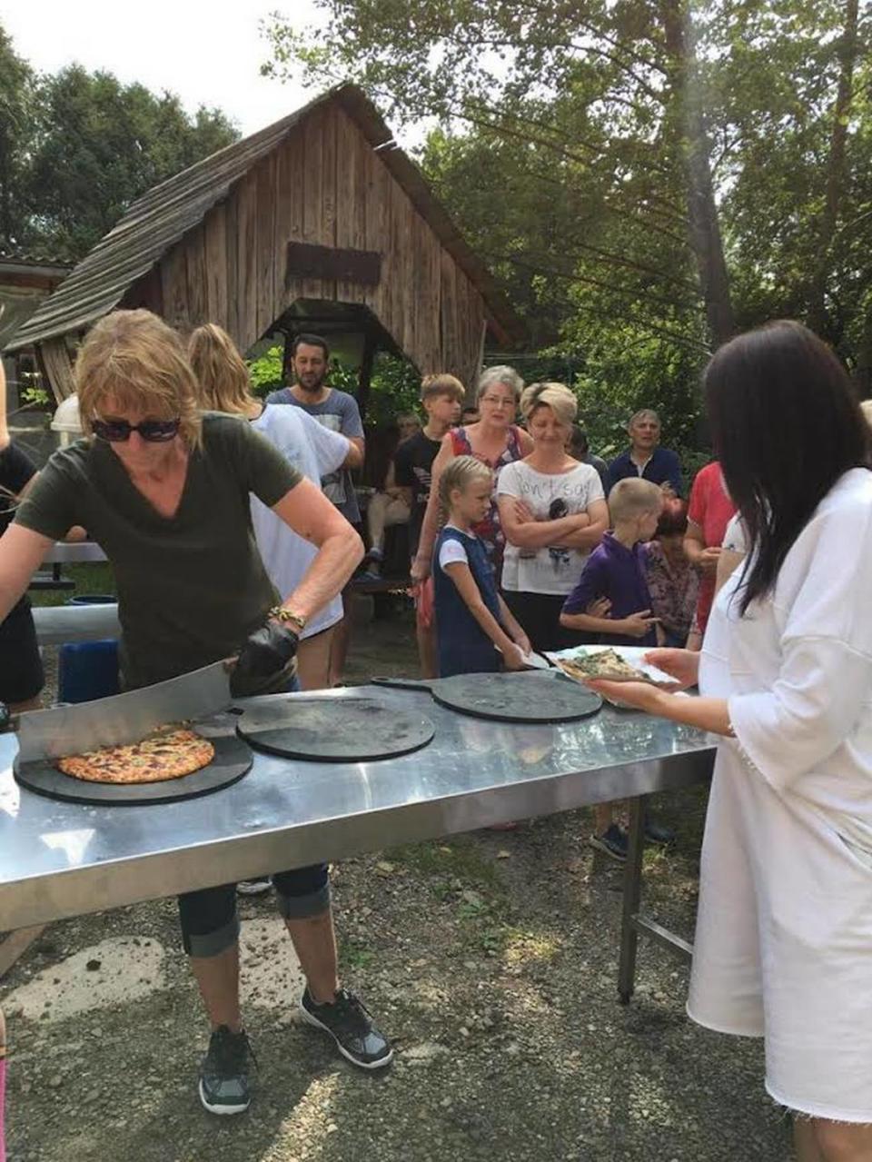 Joan Root of Lexington, wearing sunglasses, has been volunteering in the Ukraine to help families displaced by the war. She is serving Ukrainian families pizza as part of an international volunteer effort in 2023.