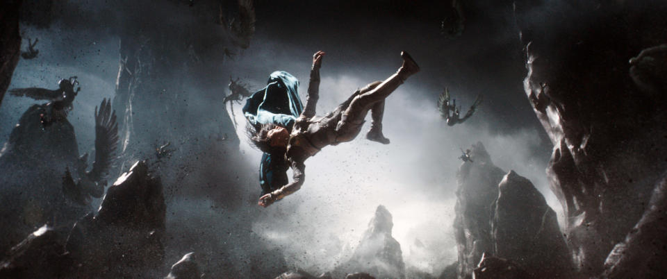 A scene from a TV show or movie depicts a person falling through a dark, rocky, and chaotic environment with other figures flailing in the background