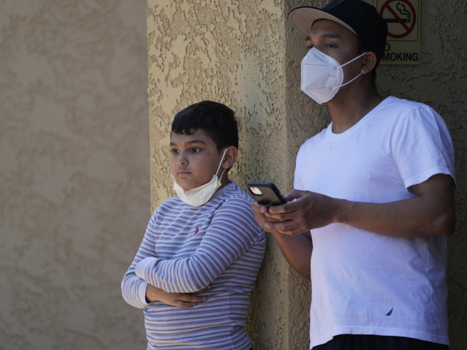 Francisco Navas with his son, Francisco, 9, stand outdoors as Los Angeles Police investigate the scene of a crime across their apartment complex in Reseda, Calif., Saturday, April 10, 2021. A woman discovered her three grandchildren, all under the age of 5, slain inside a Los Angeles apartment Saturday morning and their mother gone, police said. The mother of three children — all under the age of 5 — found slain inside a Los Angeles apartment Saturday morning has been arrested, police said. (AP Photo/Damian Dovarganes)