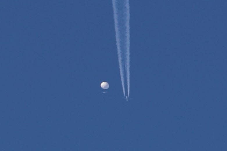 A large balloon drifts above the Kingstown, N.C., area, with an airplane and its contrail seen below it. The United States says it is a Chinese spy balloon that was moving east over America at an altitude of about 60,000 feet.