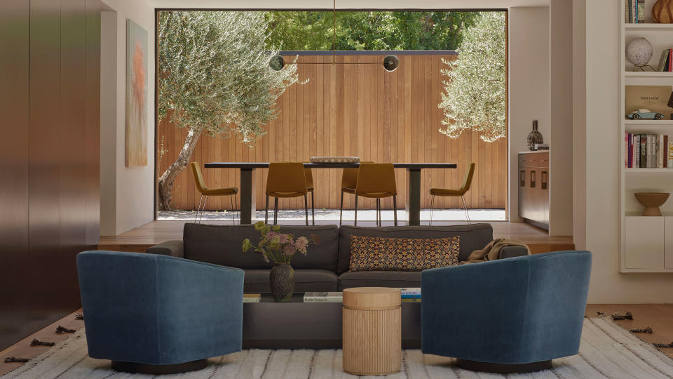 Modern living room space with blue armchairs, couch and wooden accents looking onto patio deck