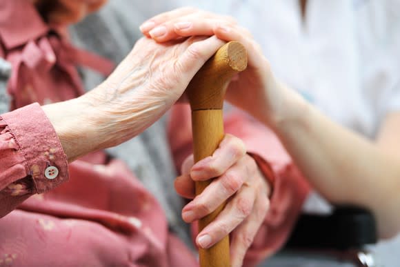 Senior citizen holding a cane and sitting with a caregiver