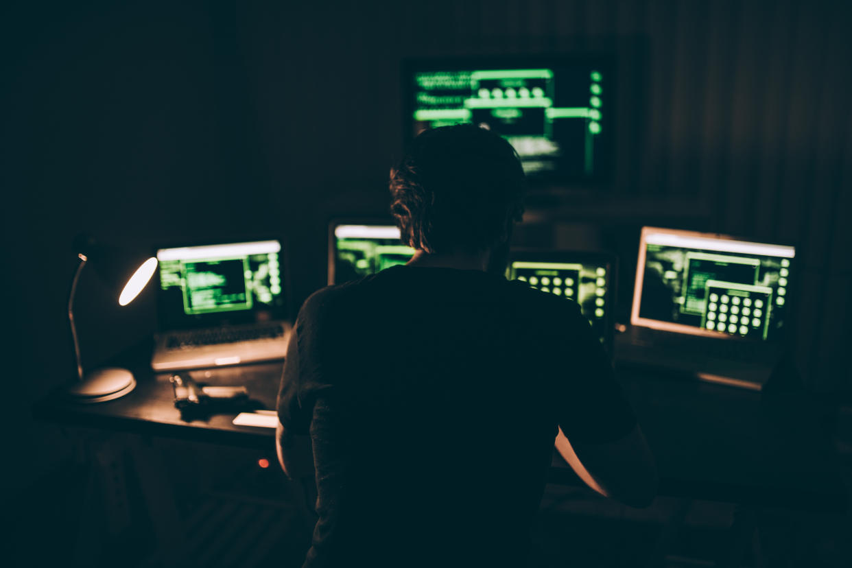 A hacker sitting in a dark room in front of lit computer screens