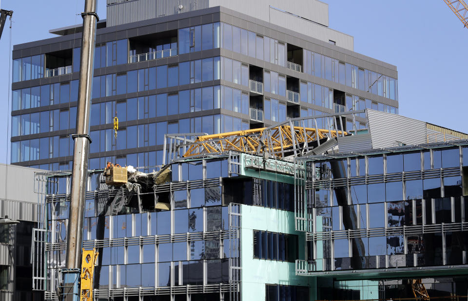 With a portion of the broken crane on the roof behind, workers suspended in a basket survey the damage left on the building when the crane atop it collapsed a day earlier, Sunday, April 28, 2019, in Seattle. The construction crane fell from a building on Google's new campus during a storm that brought wind gusts, crashing down onto one of the city's busiest streets and killing four people. (AP Photo/Elaine Thompson)