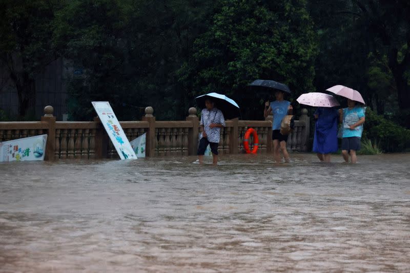 People holding umbrellas amid heavy rainfall wade through floodwaters on a bridge in Hebi