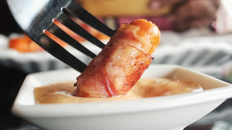 Fork dipping bacon-wrapped cocktail sausage in dip