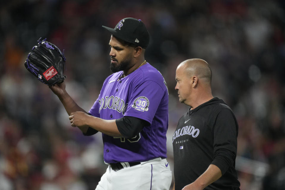 Colorado Rockies starting pitcher German Marquez, left, holds up his throwing arm as he leaves the mound with assistant trainer Heath Townsend before the sixth inning of a baseball game against the St. Louis Cardinals, Monday, April 10, 2023, in Denver. (AP Photo/David Zalubowski)