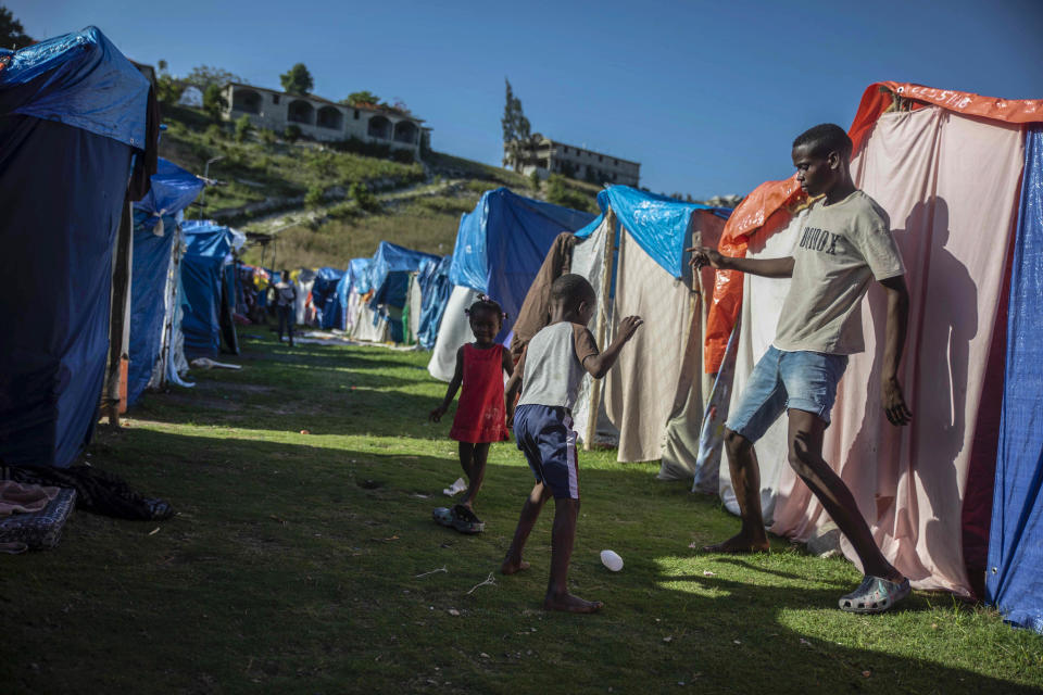 Children play at the Devirel camp in Les Cayes, Haiti, Wednesday, Feb. 16, 2022. Thousands of Haitians who lost their homes in the quake remain in camps, living in cramped shelters made of plastic and cloth sheets and corrugated metal. (AP Photo/ Odelyn Joseph)