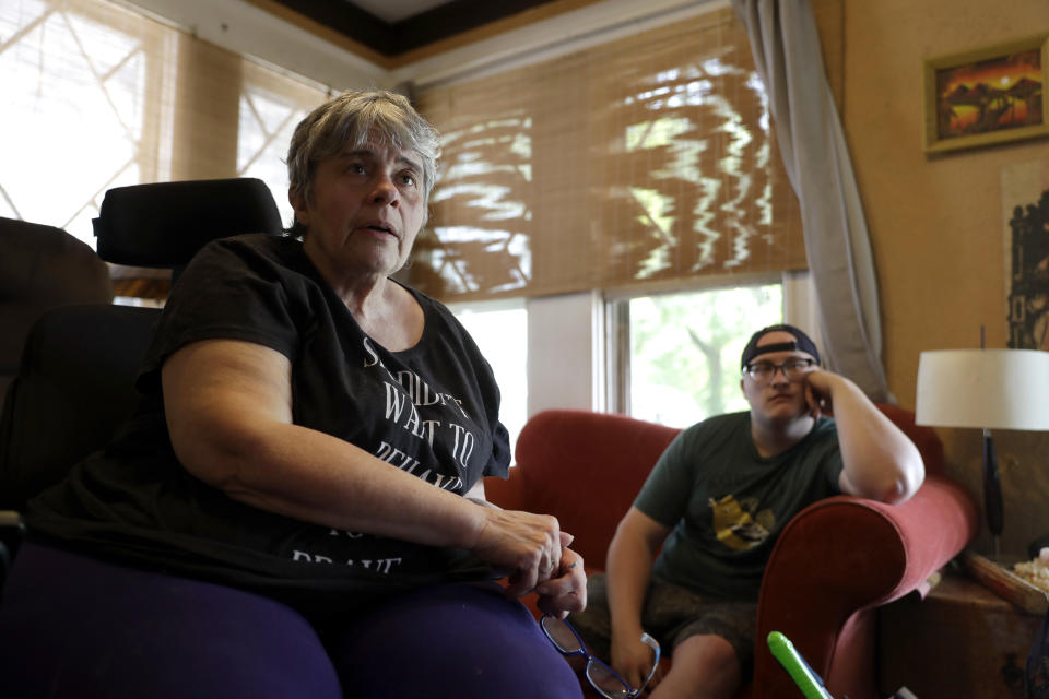 In this Tuesday, April 28, 2020, photo Debra Mize, left, and her son, Zach Stafford, watch a livestream of the daily coronavirus briefing by Illinois Gov. J.B. Pritzker on a television inside their home in Belleville, Ill. The pair say they are consuming hours of news each day in various formats about the coronavirus. Americans are grappling with an essential question as they try to get the information they need to stay safe during the coronavirus crisis: Whom do you trust? (AP Photo/Jeff Roberson)