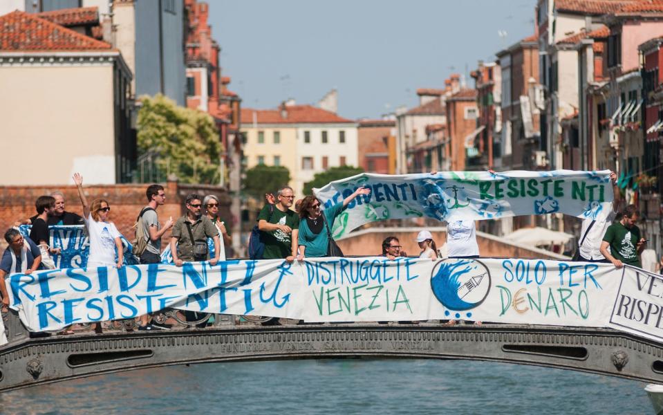 Anti-tourism protesters hang banners from a bridge in the city - Credit: GETTY