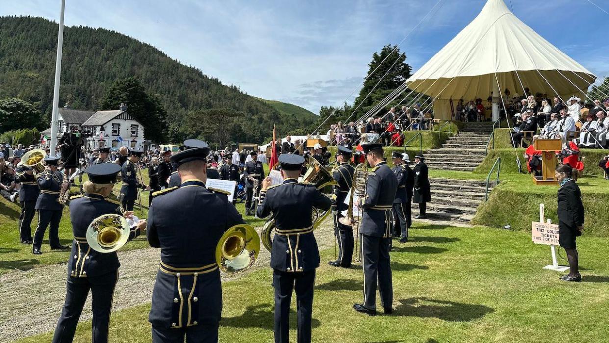 A military band playing in front of the wedding cake hill with officials sat on it.