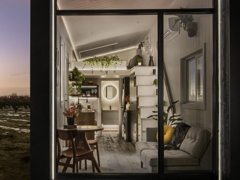 a black tiny home with a large glass wall on a snowy field at sunset