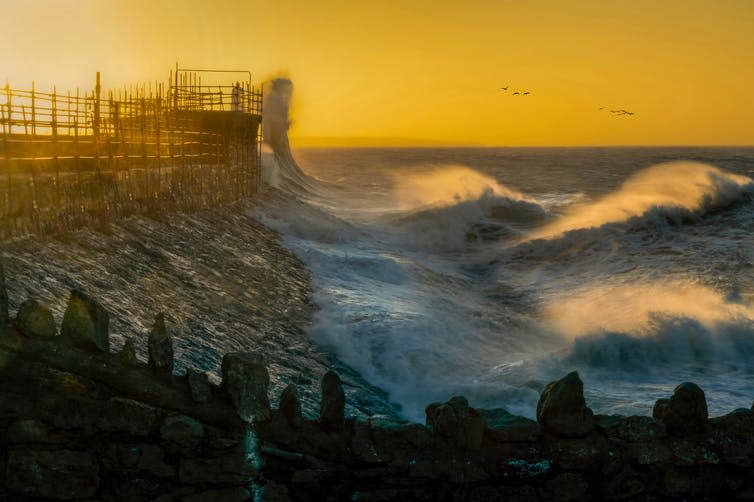 Waves crash against beach with yellow sky.