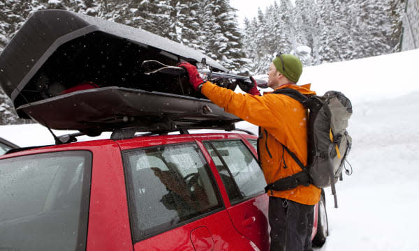 A man loading skis on top of a car.