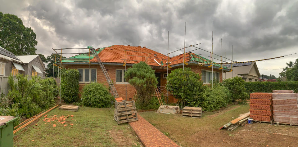 House being renovated surrounded by scaffolding and building materials.