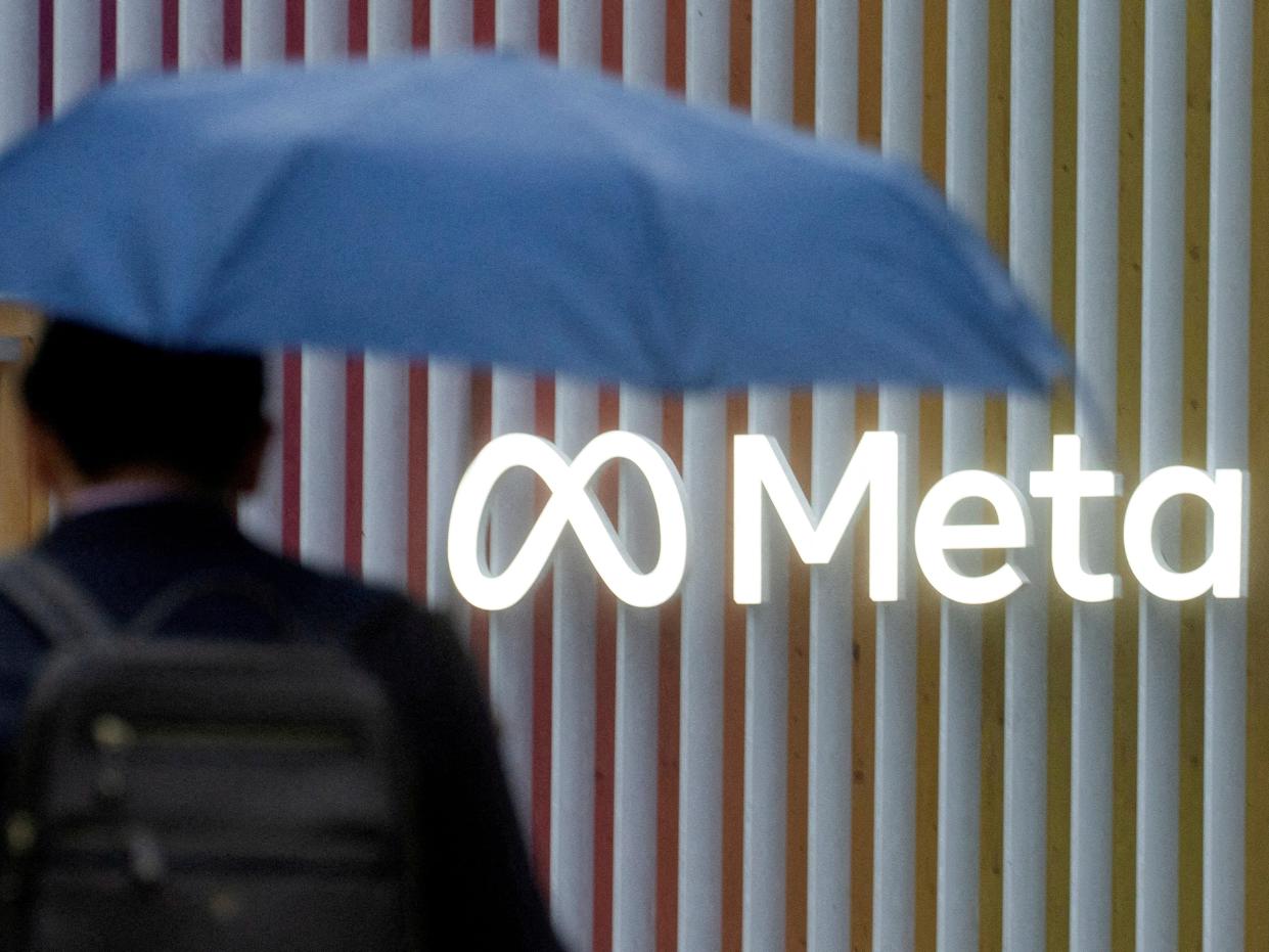 Man with blue umbrella with back against Meta logo.