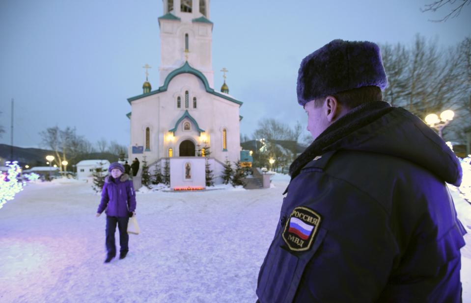 A policeman watches a believer leaving the Cathedral of the Resurrection of Christ in Yuzhno-Sakhalinsk on Sunday, Feb. 9, 2014. Law enforcement officers detained a man, who worked as a security guard, and were trying to determine why he attacked the Russian Orthodox cathedral in the city of Yuzhno-Sakhalinsk, the federal Investigative Committee said in a statement. A gunman opened fire Sunday in a cathedral on Russia's Sakhalin Island in the Pacific, killing a nun and a parishioner and wounding six others, investigators said. Concerns about security in Russia are especially high because of the Winter Olympics in Sochi, but there was no apparent connection to the games. Sakhalin Island is about 7,500 kilometers (more than 4,500 miles) from Sochi. (AP Photo/ Dmitriy Sindyakov)