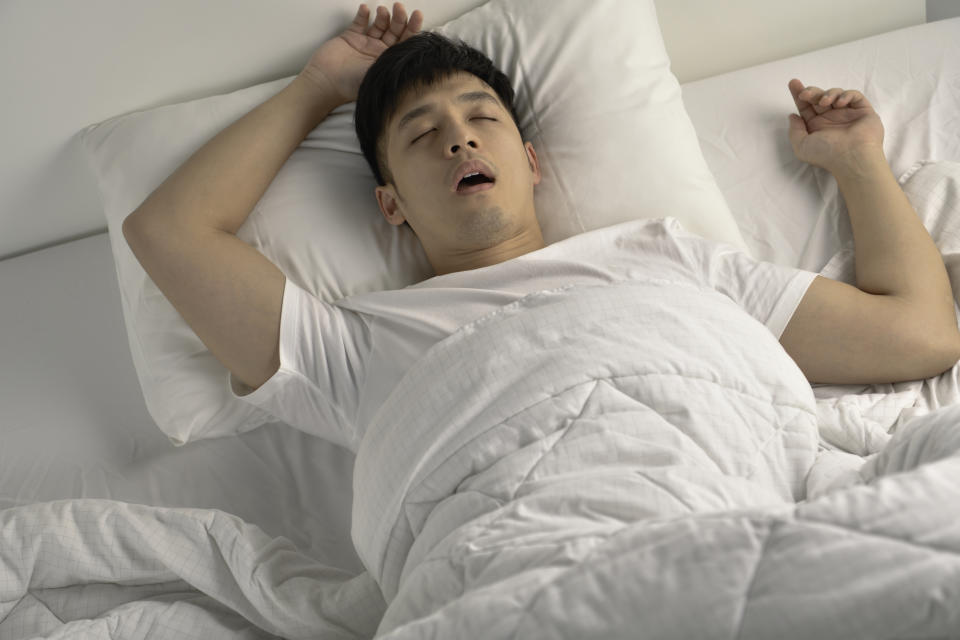 Young Asian man sleeping and snoring loudly lying in the bed