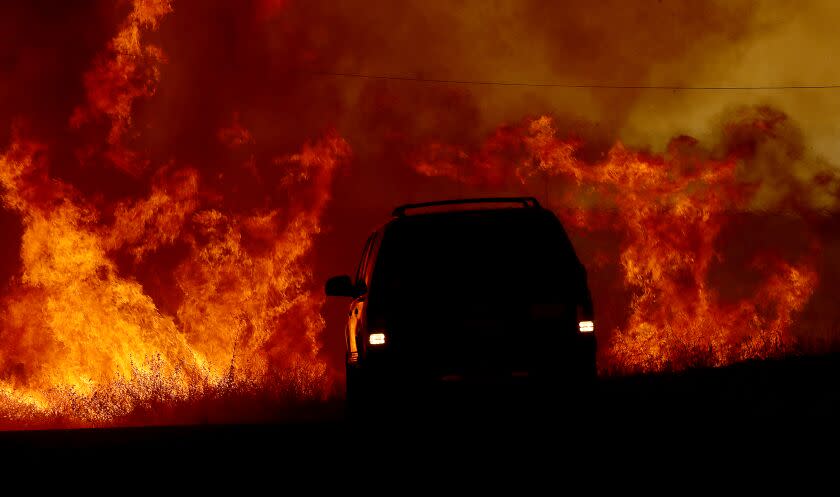 HEMET, CALIF. - SEP 6, 2022. A motorist drives past flames from the Fairview fire along Batista Road near Hemet on Tuesday, Sep. 6, 2022. (Luis Sinco / Los Angeles Times)