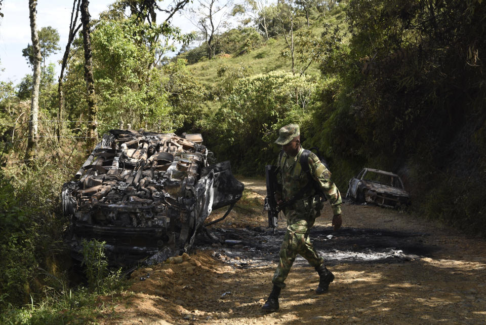 A soldier walks along the road where two vehicles where incinerated during a skirmish between illegal armed groups in which at least five people were killed in Jamundi, southwest Colombia, Friday, Jan. 17, 2020. Authorities say rebels with the former Revolutionary Armed Forces of Colombia operate in the area and may have been involved. (AP Photo/Christian EscobarMora)