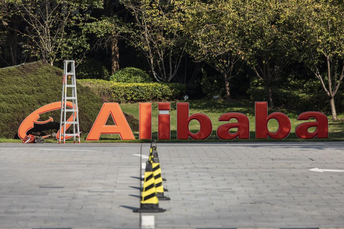  The image shows the company logo of Alibaba, a Chinese e-commerce company, with a ladder leaning against it, and text reading: 'Alibaba', in front of a landscaped area with trees.