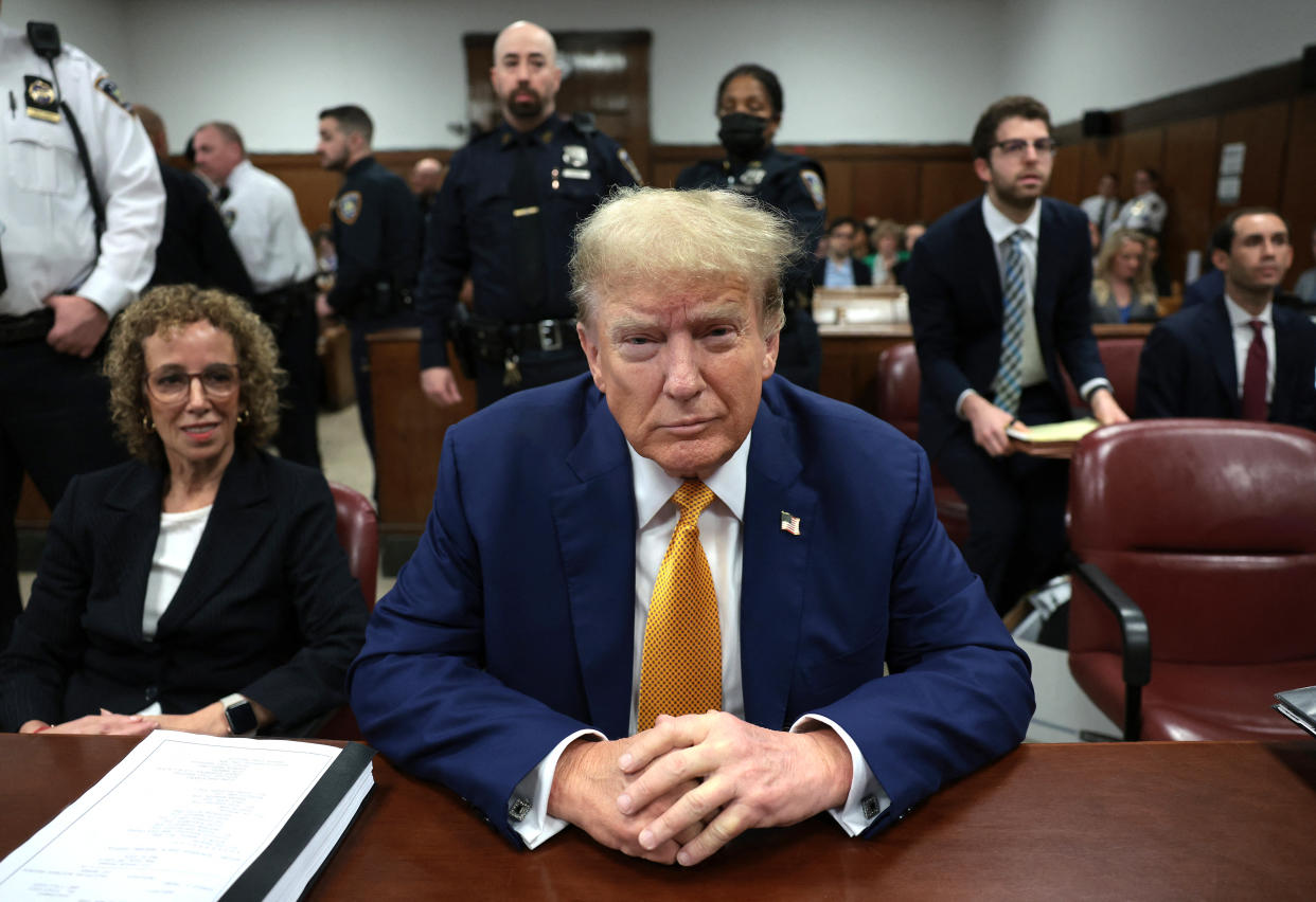 Former President Donald Trump sits at a table facing the camera surrounded by others in a courtroom.