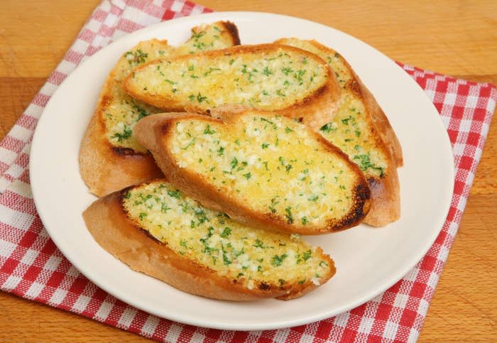 A plate of garlic bread slices on a red and white checkered tablecloth