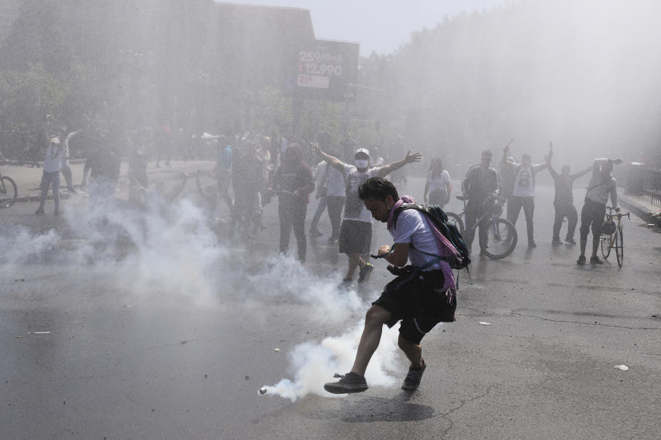 A protester kicks a tear gas canister during clashes with police in Santiago, Chile, Sunday, Oct. 20, 2019. Protests in the country have spilled over into a new day, even after President Sebastian Pinera cancelled the subway fare hike that prompted massive and violent demonstrations. (AP Photo/Esteban Felix)