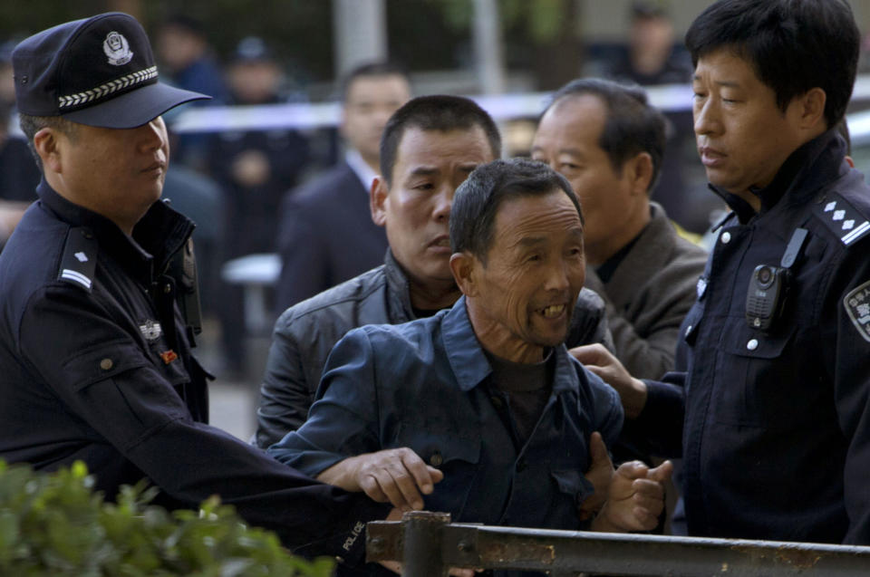 Ji Darong, center, the father of Beijing airport bomber Ji Zhongxing, is stopped by a Chinese police officer and plain clothes security personnel from approaching journalists gathered outside the Beijing Chaoyang District Court where Ji Zhongxing faced verdict and sentencing in Beijing, China, Tuesday, Oct. 15, 2013. Ji Zhongxing, a partly paralyzed man who exploded a bomb inside Beijing's airport in hopes of winning redress over an alleged beating by public officials, was given a six-year prison sentence Tuesday. (AP Photo/Ng Han Guan)