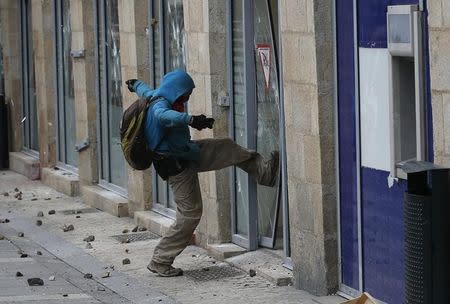 A masked and hooded youth kicks and breaks a glass door at a bank as elsewhere French high school and university students attend a demonstration against the French labour law proposal in Nantes, France, April 5, 2016. REUTERS/Stephane Mahe