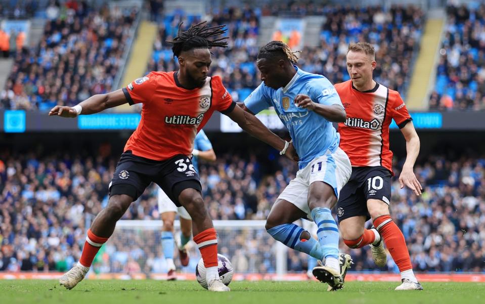 Jeremy Doku of Manchester City battles with Fred Onyedinma of Luton Town (L) and Cauley Woodrow of Luton Town (R) before scoring their 4th goal during the Premier League match between Manchester City and Luton Town at Etihad Stadium on April 13, 2024