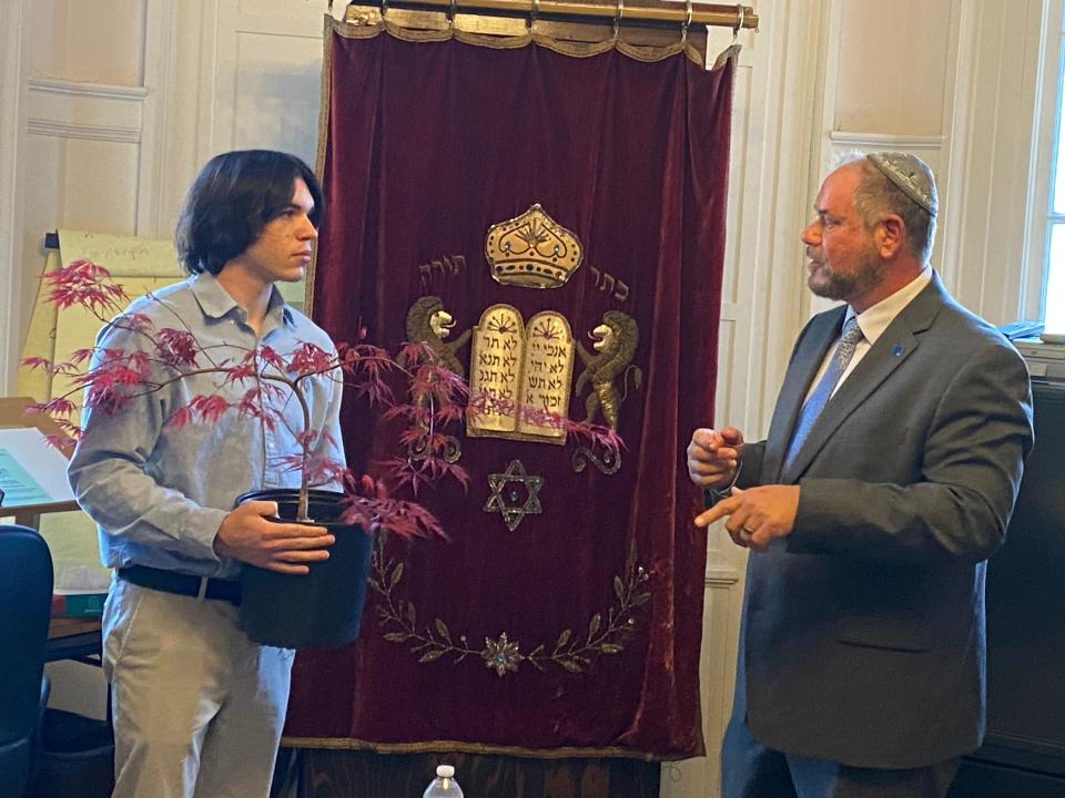 From left, Justin Andrews receives a Japanese red maple sapling from Rabbi Colman Reaboi from Congregation Agudath Achim at a ceremony at the Jewish Community House on High Street in Taunton on Monday, May 20, 2024. Reaboi told Andrews the tree has strong roots and grows out, not tall, symbolizing, in this case, Andrews' journey to "spread goodness" and "help repair a broken world" as Andrews both finds peace within himself and attempts to make further amends for spray-painting swastikas and hate slurs on the Synagogue last year. Reaboi helped prevent Andrews from severe punishment for his crimes by seeking leniency from the courts for his actions.