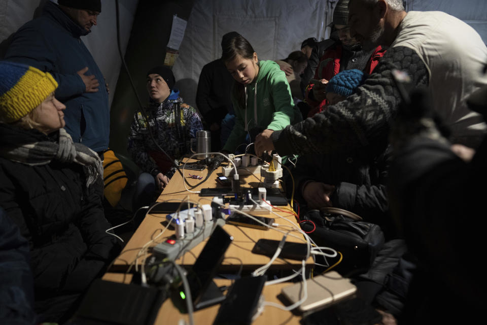 People charge their phones at a heating tent, a “Point of Invincibility,” a government-built help station that serves food, drinks and warmth, in Kherson, Ukraine, Saturday, Dec. 3, 2022. (AP Photo/Evgeniy Maloletka)