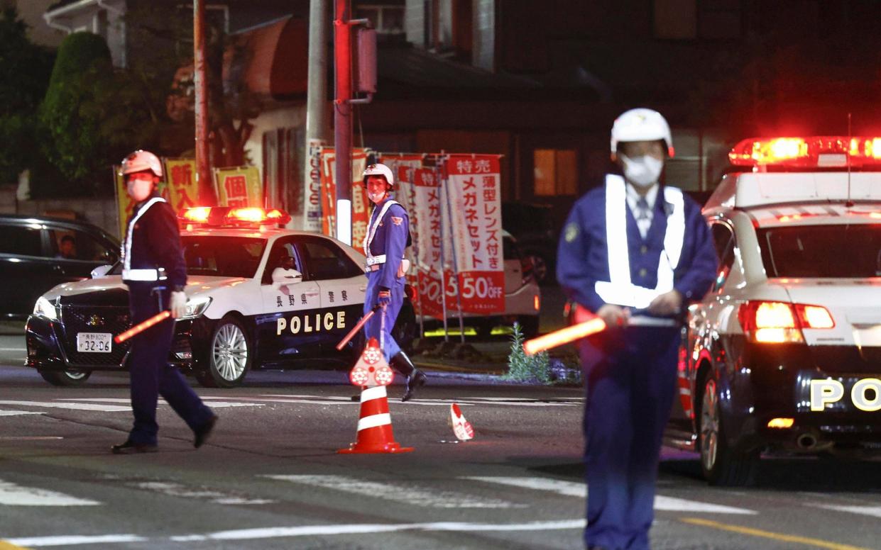 Police officers stand guard on a street near a building where a man is holed up in Nakano - AP