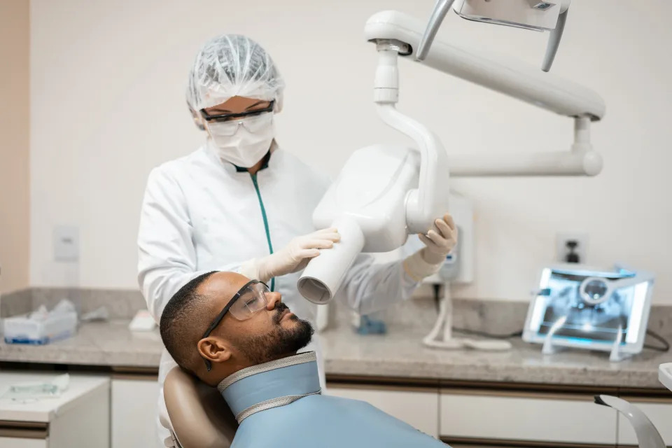 A dentist prepares a male patient for an X-ray scan in a dental clinic. The patient is wearing protective glasses and a lead apron