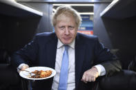 Britain's Prime Minister Boris Johnson eats a portion of pie aboard the Conservative Party campaign bus after a visit to the Red Olive catering company in Derby, central England Wednesday Dec. 11, 2019. Britain will go to the polls tomorrow Dec. 12, to vote in a pre-Christmas general election. (Ben Stansall/Pool via AP)