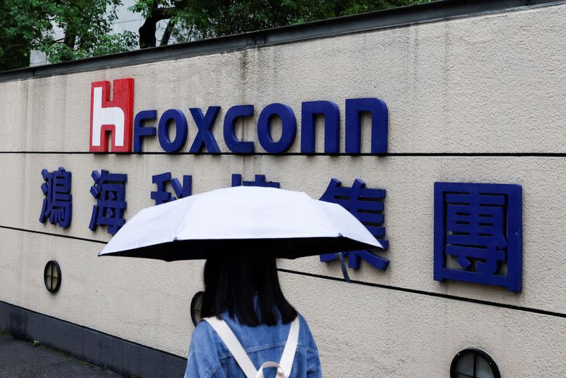 FILE PHOTO: A woman carrying an umbrella walks past the logo of Foxconn outside a company's building in Taipei