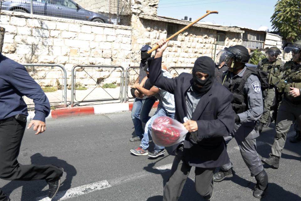 Undercover Israeli policeman holds up his walking stick as a Palestinian is arrested during clashes following Friday prayers near Jerusalem's Old City