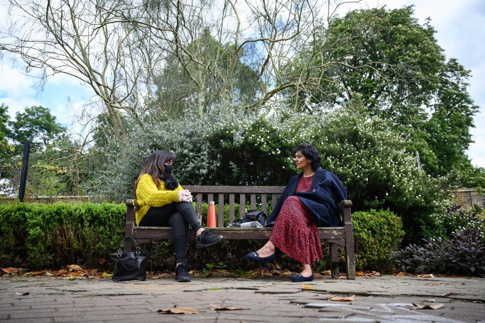 Two women chat as they sit on a bench in Golders Hill Park.