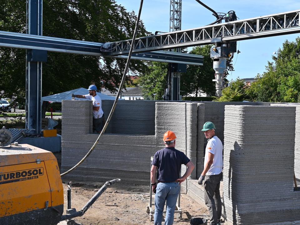 People standing near a 3D printed structure and printer.