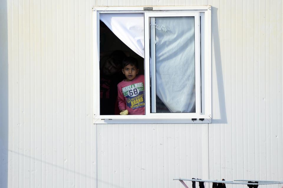 A child looks from the window of a container house at the Karatepe refugee camp before the visit of Pope Francis, on the northeastern Aegean island of Lesbos, Greece, Sunday, Dec. 5, 2021. Pope Francis is returning to Lesbos, the Greek island that was at the heart of a massive wave of migration into Europe six years ago, after making pointed criticism of European governments on the handling of the crisis during a visit to two hard-hit countries. (AP Photo/Alessandra Tarantino)