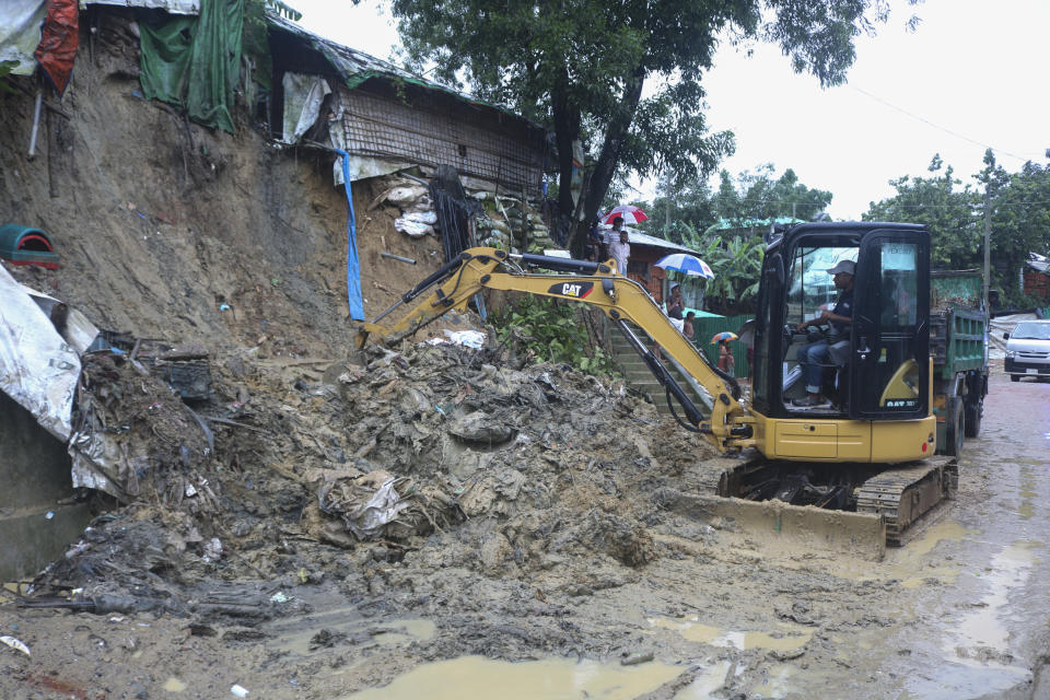 Rohingya refugees and others look on as machinery is used to remove debris after a landslide triggered by heavy rains in a camp at Ukhiya in Cox's Bazar district, Bangladesh, Tuesday, July 27, 2021. (AP Photo/ Shafiqur Rahman)