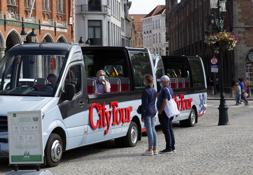 A tour operator in a protective face mask sits in an empty tour bus as he speaks with a couple on the market square of Bruges, Belgium, Monday, Aug. 24, 2020. Europe’s leanest summer tourist season in history is starting to draw to a close, six months after the coronavirus hit the continent. COVID-19 might tighten its grip over the coming months, with losses piling up in the tens of billions of euros across the 27-nation European Union. In the Belgian city of Bruges, white swans instead of tourist boats rule the canals, hotels stand empty and museums count their losses. (AP Photo/Virginia Mayo)