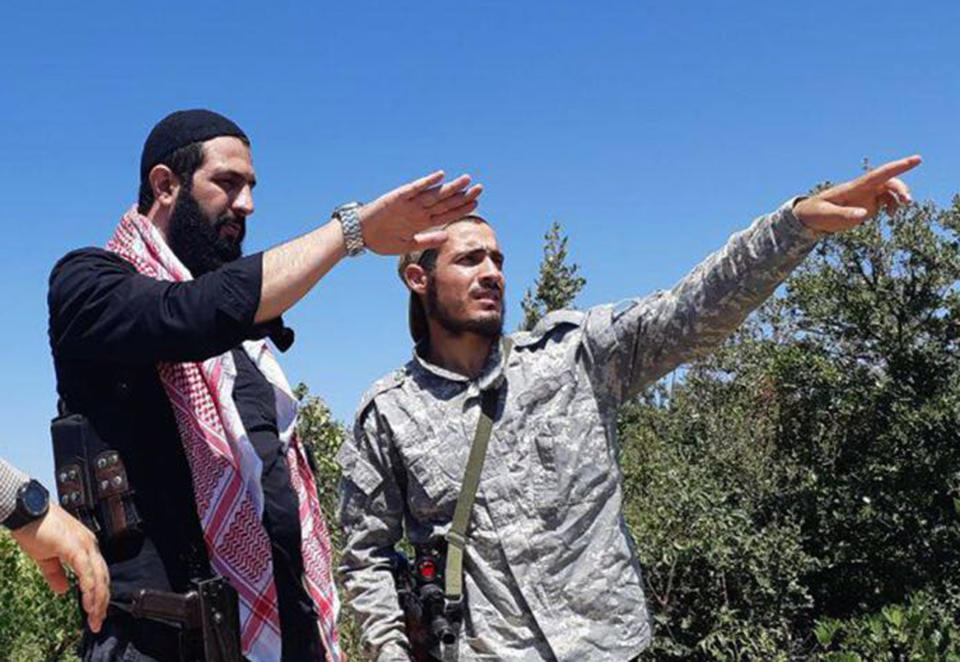 This undated photo released by the militant group Levant Liberation Committee on Tuesday, Aug. 21, 2018, shows Abu Mohammed al-Golani of the militant Levant Liberation Committee and the leader of Syria's al-Qaida affiliate, left, talking with a fighter, in the countryside of Latakia, Syria. Al-Golani vowed to fight on in Idlib province, the country's last major rebel stronghold, in the face of a possible government offensive in a video posted online to mark the Muslim feast of Eid al-Adha, shortly before midnight Tuesday, Aug. 22, 2018. (Militant UGC via AP)