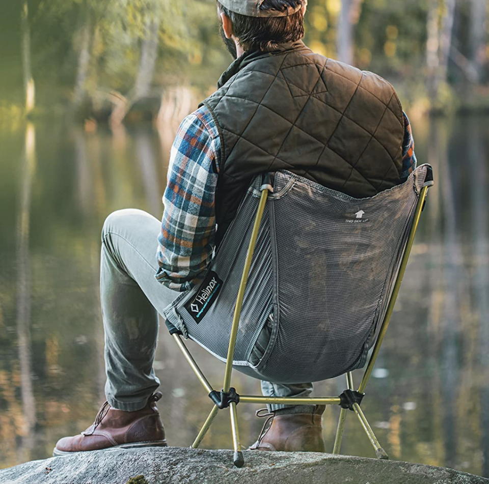 man sitting on Helinox Chair Zero outside while camping (Photo via Amazon)