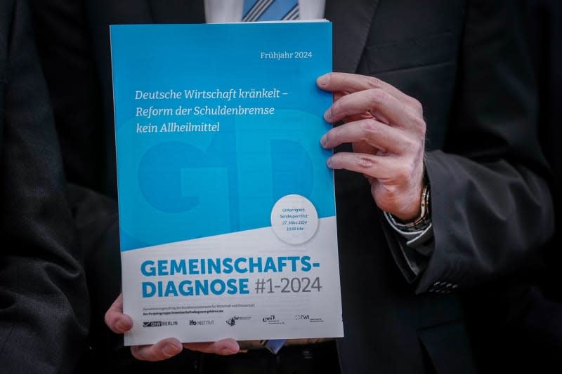 Stefan Kooths, Kiel Institute for the World Economy (IfW Kiel), shows the booklet with the joint forecast of the economic research institutes for spring 2024 at the Federal Press Conference. Kay Nietfeld/dpa