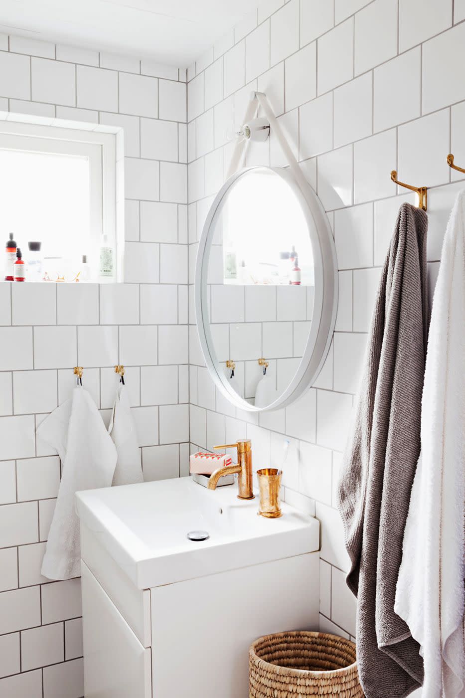 bathroom storage ideas, white bathroom with a circle mirror and small towels hanging from hooks on the tile wall
