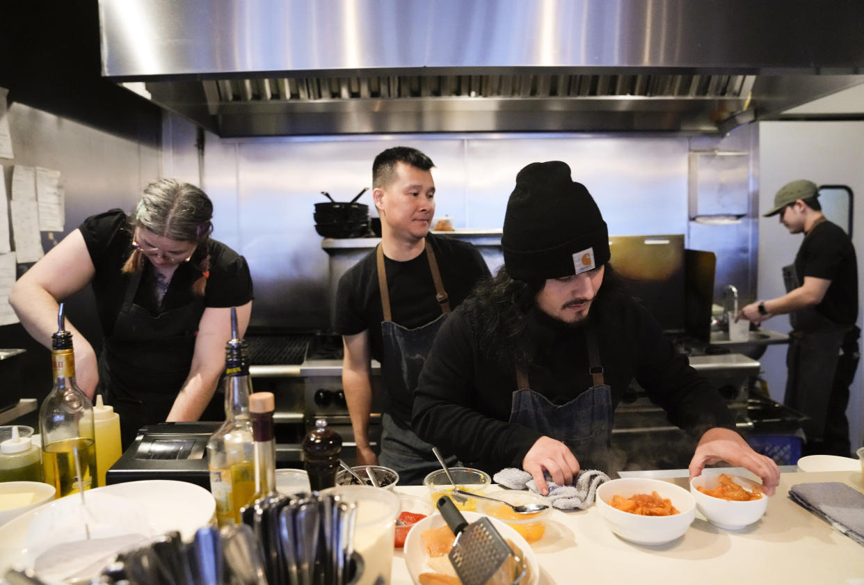 Santos Enrique Camara, 27, who dropped out of Shoreline Community College at age 19 in 2015, plates pasta at Capers + Olives as Shennandoah Utsler, left, and chef Jimmy Liang work behind him Friday, March 24, 2023, in Everett, Wash. When Camara arrived at Shoreline Community College to study audio engineering, he quickly felt lost. “It’s like a weird maze,” remembered Camara, who had finished high school with a 4.0 grade-point average. “You need help with your classes and financial aid? Well, here, take a number and run from office to office and see if you can figure it out.” (AP Photo/Lindsey Wasson)